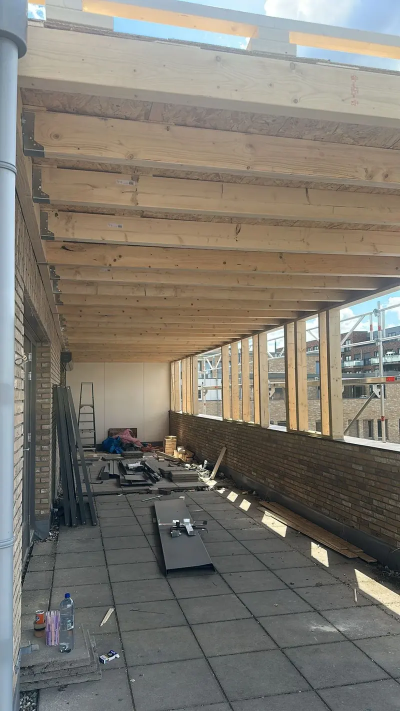 Dakopbouw in aanbouw in Rotterdam: houten balklaag en houtskeletwand op het bestaande platte dak, met de kozijnopeningen al uitgespaard